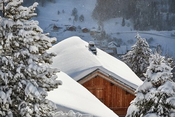 Wall Mural - House roof covered with falling snow in a beautiful mountain scenery, idyllic winter atmosphere