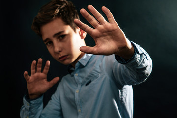 The concept of domestic violence. Sad teenager puts his hands in front of him defending himself from the threat of attack. Black background