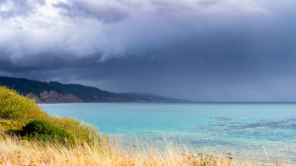 The calm before the storm; Clear and calm turquoise water on the Pacific Ocean coastline, with menacing storm clouds visible in the background; Ano Nuevo State Park, Pescadero, California