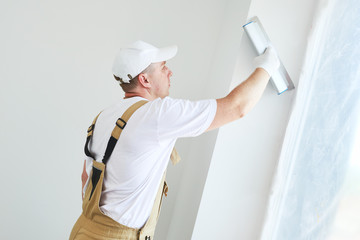 Wall Mural - Painter with putty knife. Plasterer smoothing esconson surface at home renewal