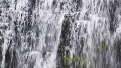 Wall Mural - Water splashes and cascades down a beautiful waterfall flowing over a rock face in this seamless video loop