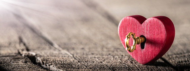 Wall Mural - small rustic red heart with shiny golden key standing on wooden table - valentine's day concept