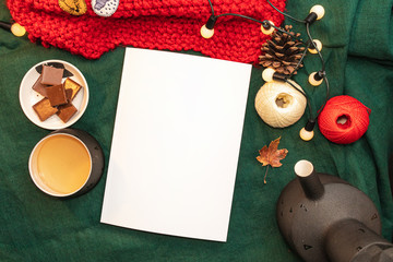 Christmas mockup, with a postcard, wishes, letter on the blanket with a kettle, leaf, tea, cone, chocolate and xmas tree lights.  Background top view blank space for text.