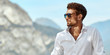 Portrait of handsome man wearing elegant white shirt and sunglasses, standing near the lake in the alps