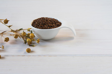 Flax seeds in a white ceramic spoon and shoot of dry flax with fruits on a light background. Omega 3 Acids