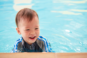 Wall Mural - Asian 2 years old toddler boy child on the edge of a swimming pool, little kid takes a swimming lesson in indoor swimming pool