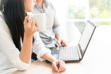 A white coffee cup in the hands of a businesswoman while talking business with a laptop computer.