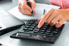 Female Accountant In The Office Uses A Calculator And Writes Data In A Notebook. Profit Analysis, Taxes And Payments Calculations, Preparation Of Financial Statements Concept