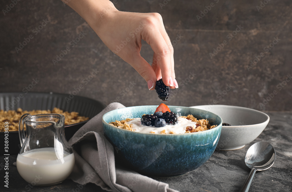 Woman preparing tasty granola with yogurt on grey background