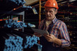 © AnnaStills - Serious mature foreman in work helmet working online on tablet pc while standing near the shelves with metal pipes