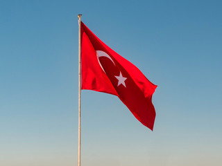 Turkish flag is waving on the top of the flagpole against bright clear blue sky at the background