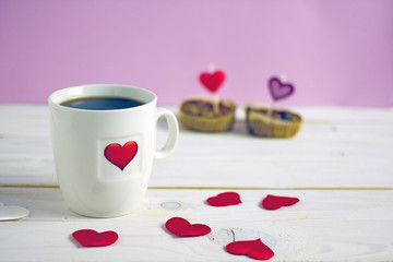 Canvas Print - Valentine's Day breakfast. White mug of tea with a heart pattern and and two homemade cupcakes with candle hearts on a pink background. Copy space