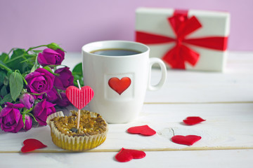 Canvas Print - Valentine's Day breakfast. White tea mug with a heart pattern and  homemade cupcake with candles, hearts next to a bouquet of roses and a box with a gift on a wooden table. Copy space