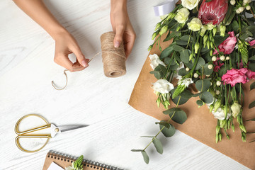 Wall Mural - Florist making beautiful bouquet at white wooden table, top view