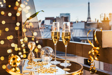 Celebration Of New Year Or Christmas Concept. Two Glasses With Champagne And Golden Decorations On A Balcony With A View On Rooftops And Eiffel Tower.