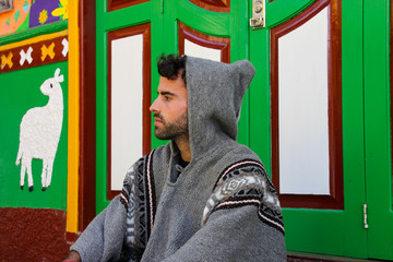 Man with hood and poncho sitting in front of colorful door