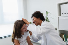 Woman Afro American Doctor General Practitioner Examining Ear Of A Ill Child. Ear Infections.