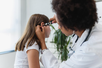 Woman afro american doctor general practitioner examining ear of a ill child. Ear infections.