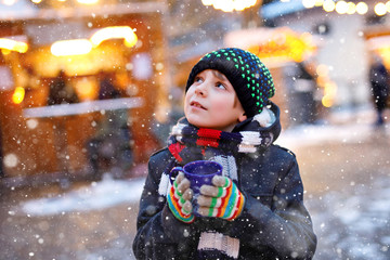 Wall Mural - Little cute kid boy drinking hot children punch or chocolate on German Christmas market. Happy child on traditional family market in Germany, Laughing boy in colorful winter clothes