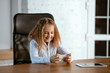 © master1305 - Portrait of young caucasian girl looks dreamful, cute and happy. Looking up, sitting indoors at the wooden table with tablet and smartphone. Concept of future, target, dream to buy, visualisation.