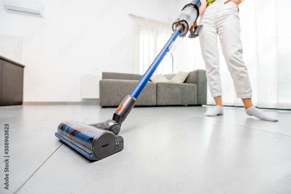 Woman cleaning floor with cordless vacuum cleaner in the modern white living room. Concept of easy cleaning with a wireless vacuum cleaner - obrazy, fototapety, plakaty 