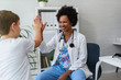 © lordn - Smiling female afro american doctor general practitioner talks and amuses child before medical examination