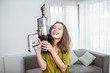 Portrait of a young and happy woman with cordless vacuum cleaner, enjoying housework at home. Concept of an easy cleaning with wireless tools