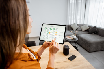 Young woman controlling home with a digital touch screen panel. Concept of a smart home and mobile application for managing smart devices at home