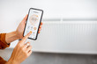 © rh2010 - Controlling radiator heating temperature with a smart phone, close-up with radiator on the background. Concept of a smart home and mobile application for managing smart devices at home