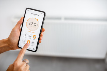 Controlling radiator heating temperature with a smart phone, close-up with radiator on the background. Concept of a smart home and mobile application for managing smart devices at home