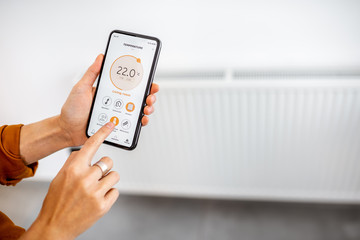 Controlling radiator heating temperature with a smart phone, close-up with radiator on the background. Concept of a smart home and mobile application for managing smart devices at home