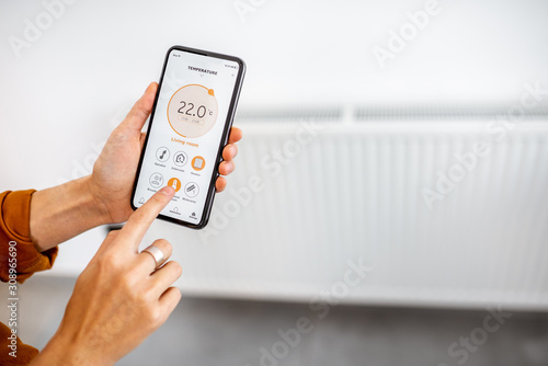Fotomural Controlling radiator heating temperature with a smart phone, close-up with radiator on the background