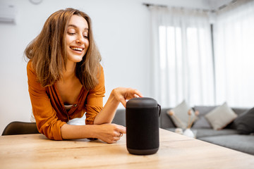 Wall Mural - Young woman turning on wireless smart column at home. Concept of a smart home wireless devices. Concept of smart home and voice command control