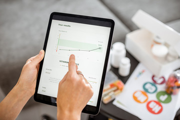 Woman checking the result of medical tests on a digital tablet, close-up with nutritional supplements on the background. Concept of individual online selection of food supplements