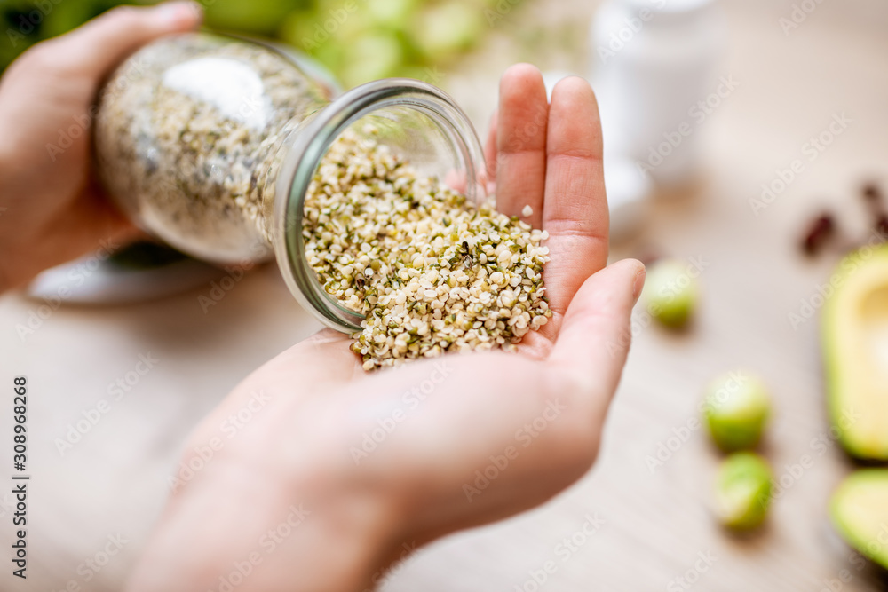 Holding hemp seeds at the table with healthy vegan food ingredients and supplements, top view. Concept of Marijuana as a new trend in food and cosmetic industry - obrazy, fototapety, plakaty 