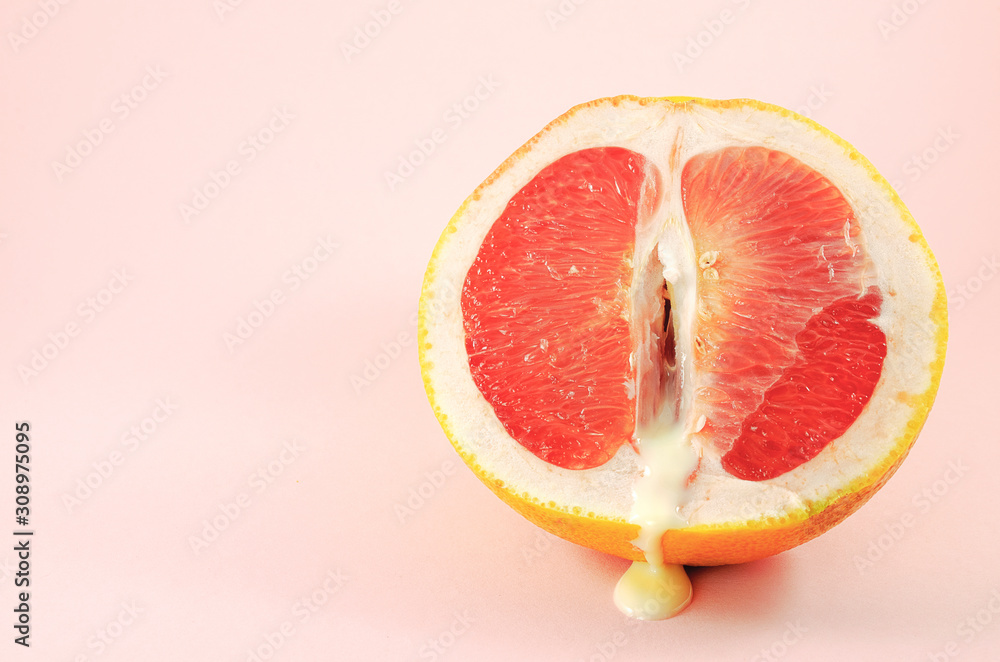Sexy grapefruit with sperm, erotic concept. Sectional grapefruit is a symbol of the vagina and clitoris. Half grapefruit with dripping white liquid on a pastel background. Erotic concept. - obrazy, fototapety, plakaty 