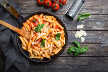 Penne Pasta In Tomato Sauce And Cheese Decorated With Basil On A Wooden Background, Top View