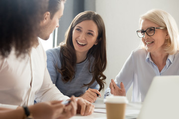 Wall Mural - Diverse employees laugh talking sitting at desk in office