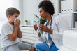 © lordn - Woman African American doctor general practitioner helping child to put nebulizer inhaler face mask. Asthma treatment for children.