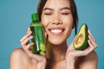 Wall Mural - Portrait of half-naked asian woman holding avocado and bottle of lotion