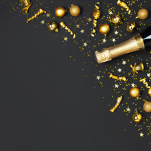 Christmas And New Year Background. Champagne Bottle, Golden Christmas Balls, Festive Ribbons, Star Confetti On Black Background Top View. Flat Lay Holiday Card. Party Concept Festive Decorations 2020