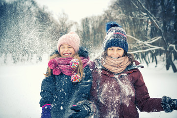 Little girl and her mother playing outdoors at winter day. Active winter holydays concept.