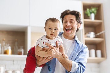 Wall Mural - Cheerful daddy riding his baby son like plane, kitchen interior