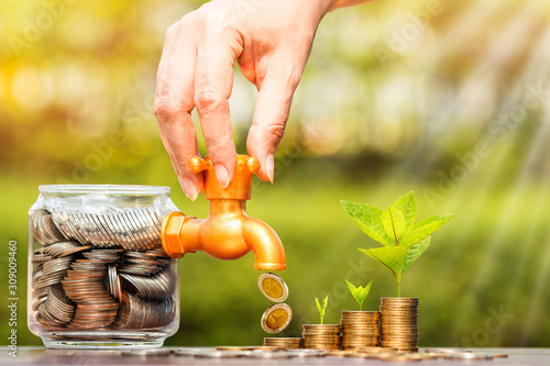 Fotomural Woman's hand open a faucet of jar and gold coin drop for invest with growing money and seed put on the wood in the public park, for currency and financial business investment and fund concept