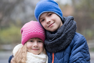 Two children boy and girl hugging each other outdoors wearing warm clothes in cold autumn or winter weather.