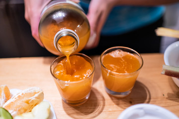 Woman person serving pouring kombucha fermented tea into two juice shot glasses on wooden table from bottle