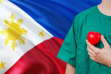 Philippines Veterinary Clinic Concept. Veterinarian Is Holding Plastic Heart In Green Uniform On National Flag Background. Animial Love Theme.