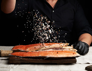 Wall Mural - chef in a black shirt and black latex gloves prepares salmon fillet on a wooden cutting board