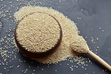 Dry organic quinoa grains in wooden bowl and spoon on dark stone background. Cooking ingredients, healthy food.