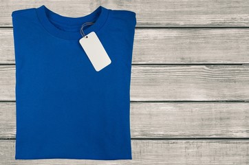 Wall Mural - Blue T-shirt with a tag on wooden desk